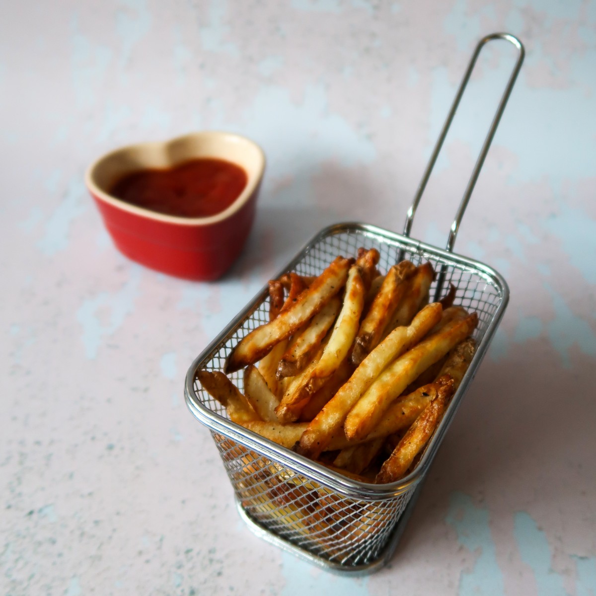Healthy Airfryer chips in a fries basket with a heart shaped ramekin of tomato ketchup