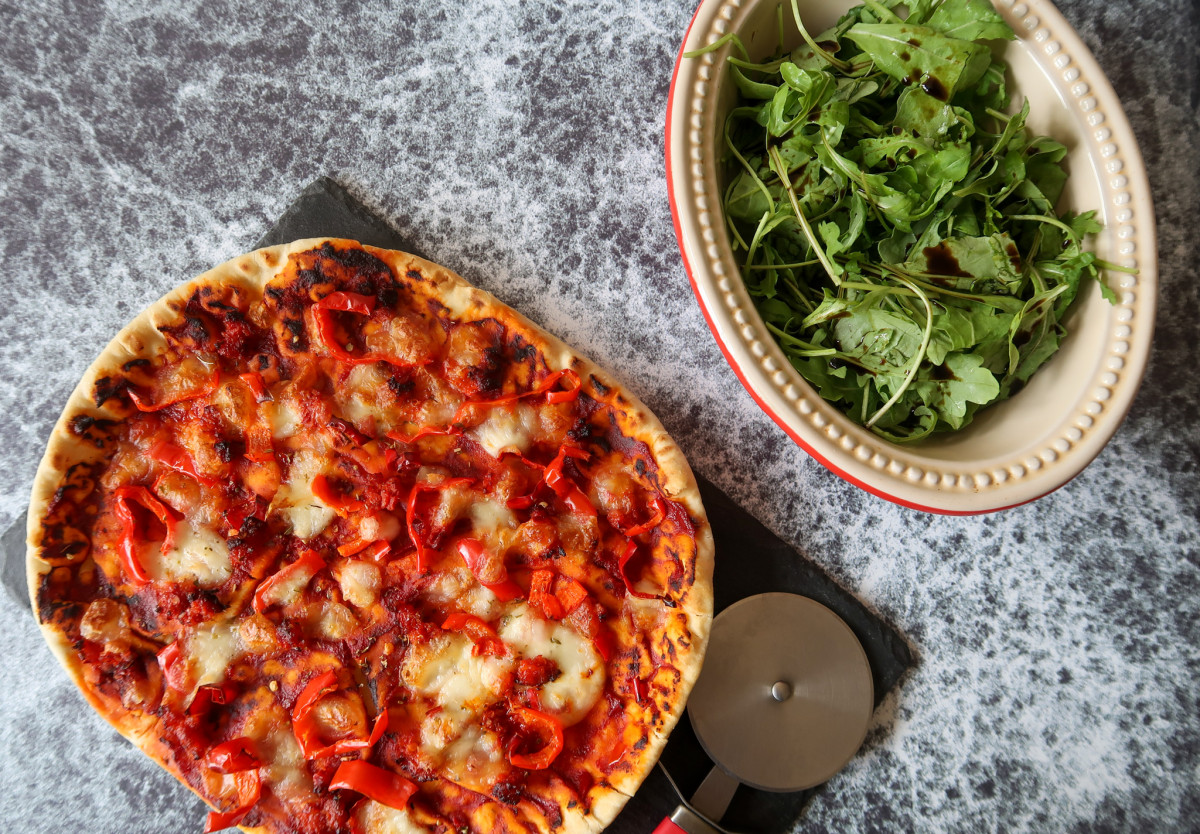 An air fryer pizza made using pizza dough made in the bread maker served with rocket and balsamic dressing alongside a piece of slate and a pizza cutter