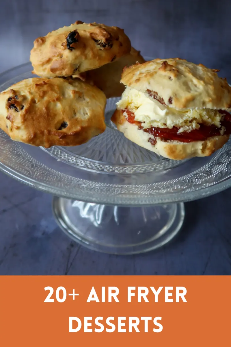 A stack of three fruit scones on a glass cake dish, alongside one fruit scone that has been sliced in half and dressed with cream and fruit jam, with text underneath that says 20+ air fryer desserts