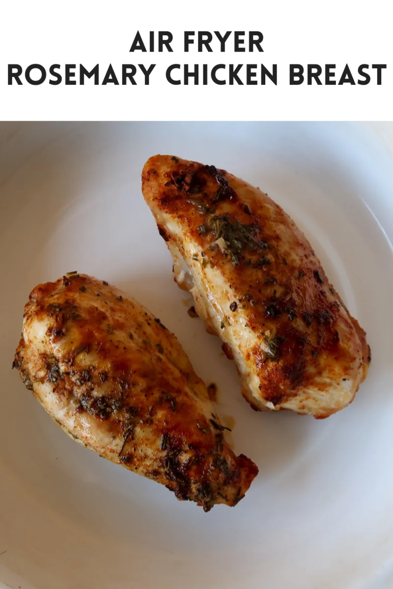 Two chicken breasts that have been dressed with paprika, chopped rosemary, garlic and olive oil and cooked in the air fryer. The chicken breasts are in a white enamel dish