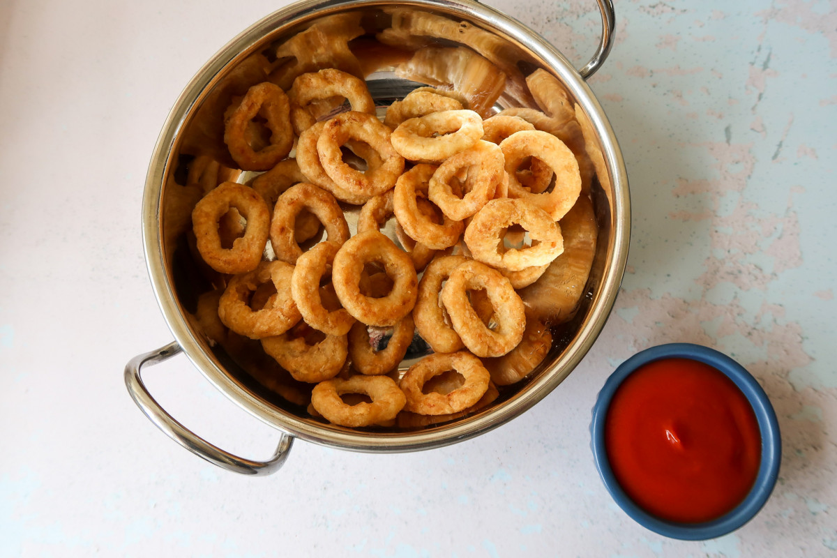 Air fryer frozen onion rings in a metal bowl with a blue dish of tomato ketchup to the side