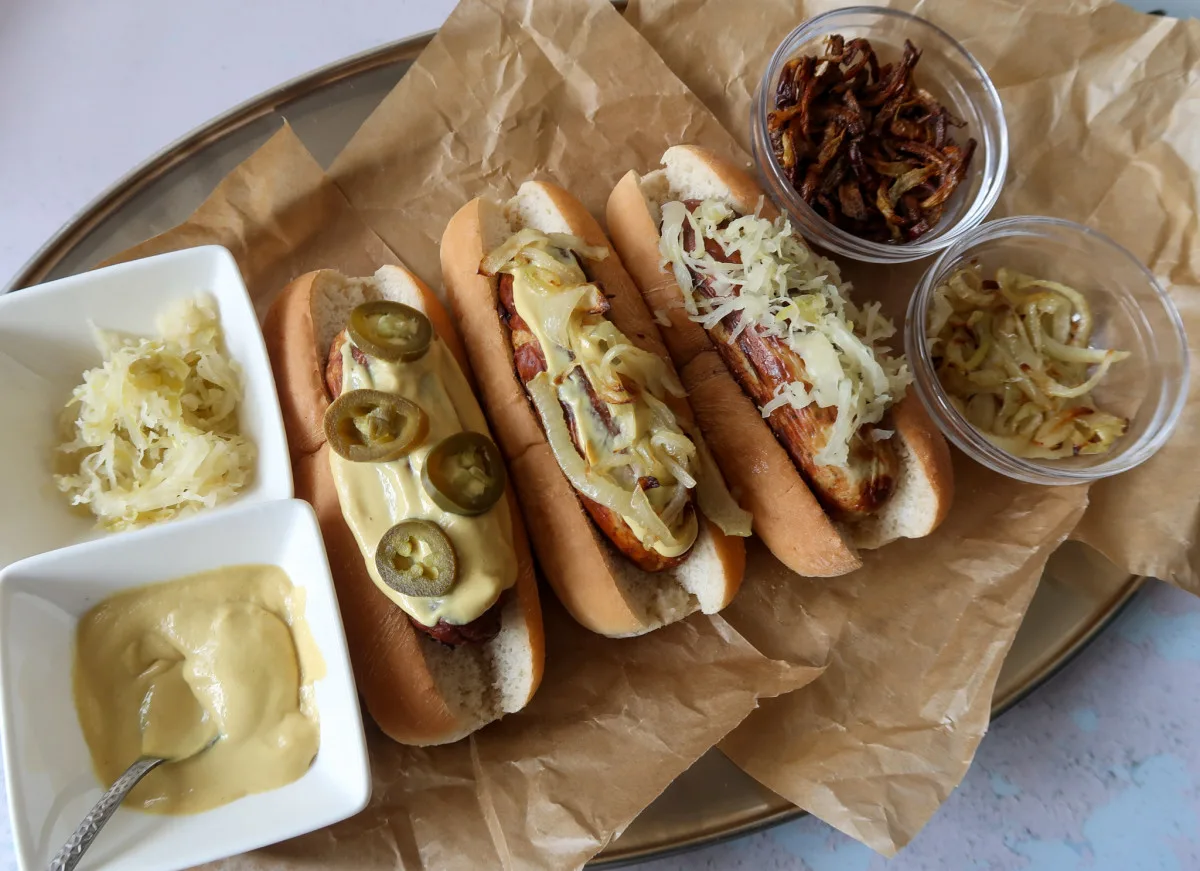 Cooked air fryer bratwurst in buns, with air fryer onion rings, grilled and crispy onions and stoneground mustard. The Bratwurst (3) are dressed with sauerkraut, dressed with mustard and onions and dressed with mustard and jalapeños