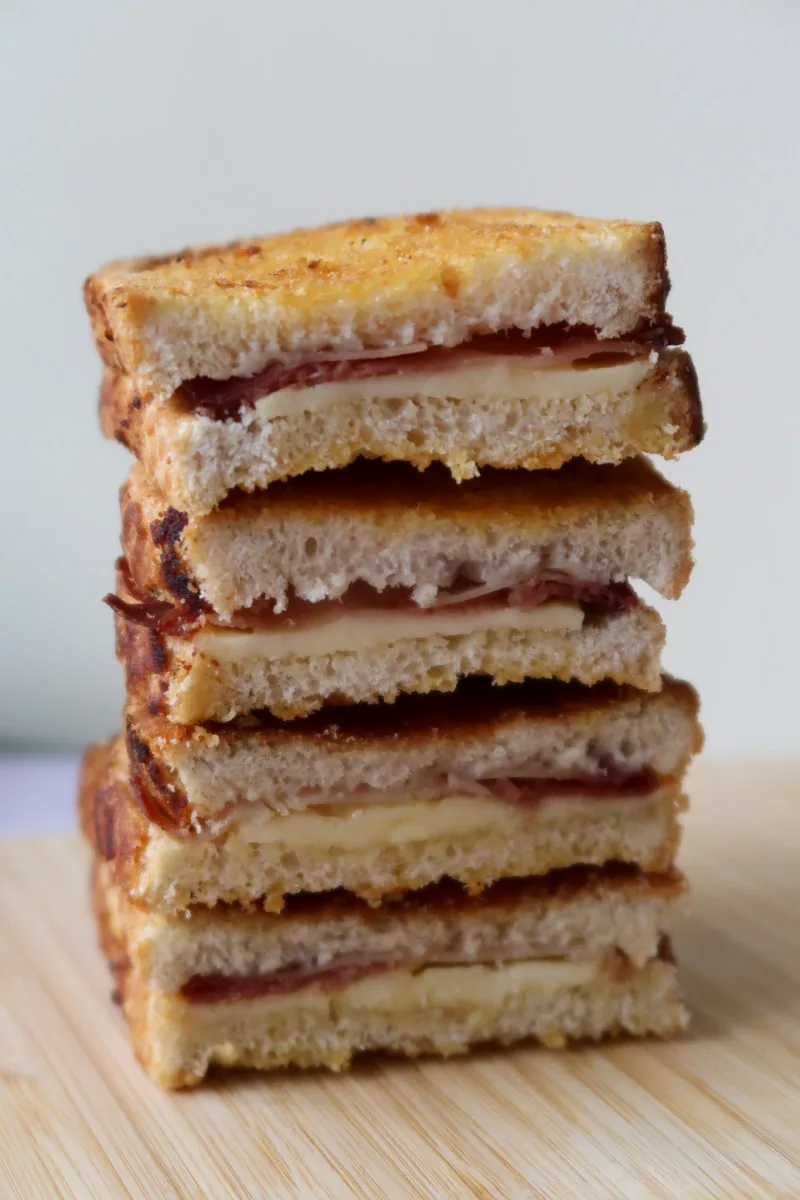 Air fryer grilled ham and cheese sandwiches cut in half and stacked up on a wooden chopping board
