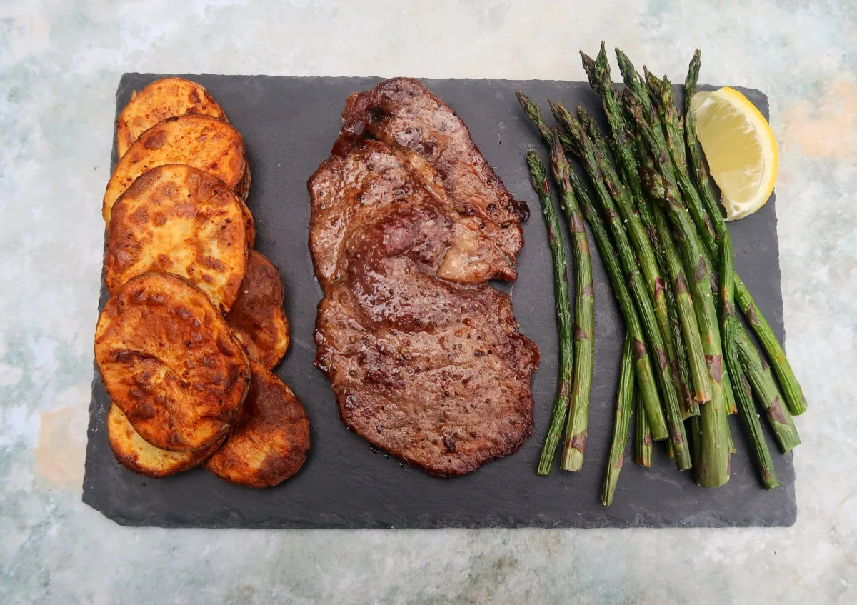 Air fryer ribeye steak with sliced potatoes and asparagus.